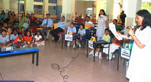 Quiz host Ms Melissa asking questions to the participants with Mr Bodhankar and Mr Winston watching the competition in progress